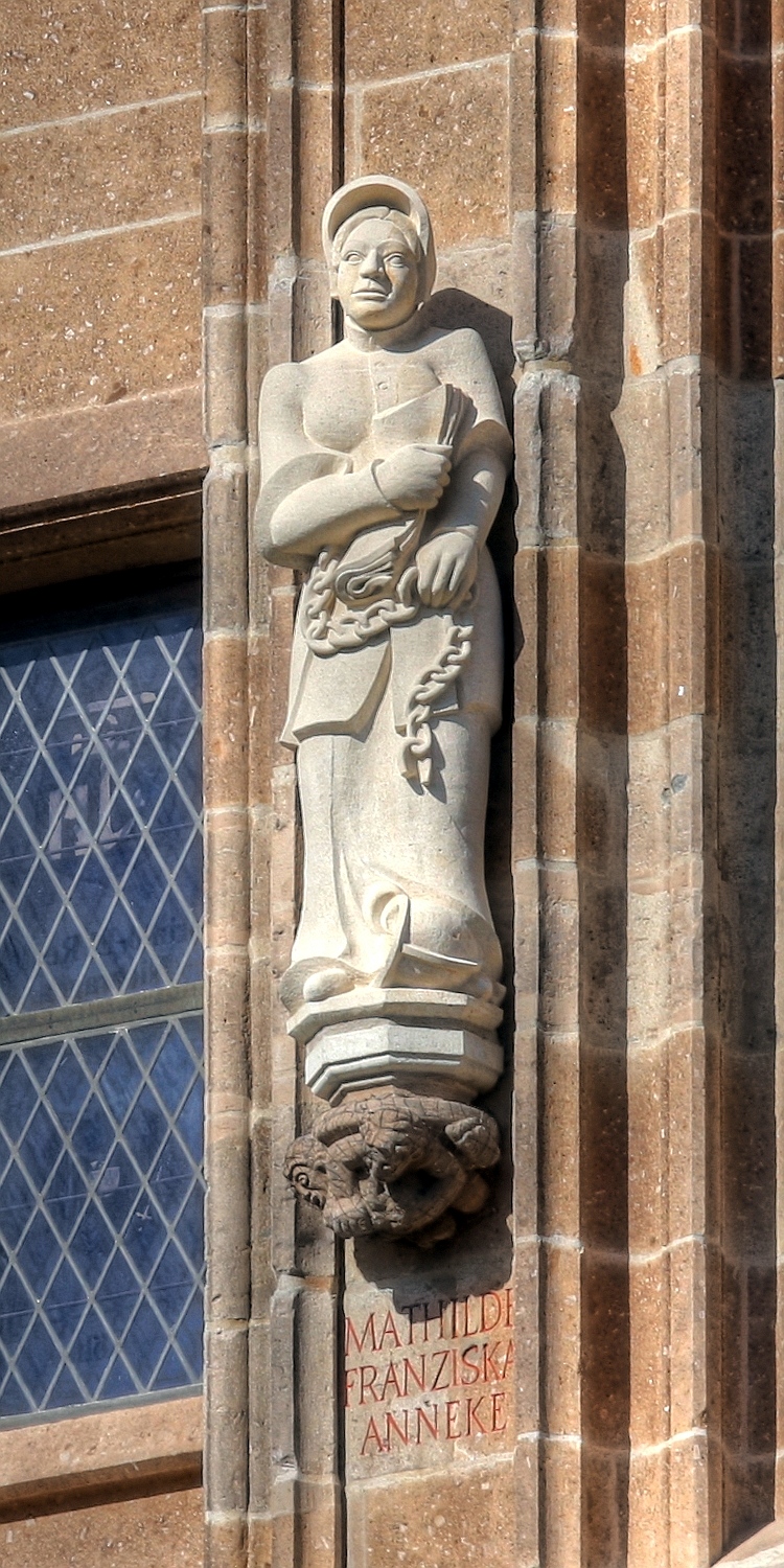 Rathausturm Köln mit der Figur der Mathilde Franziska Anneke Details zu der Statue: Bildhauer der Anneke-Statue: Katharina Hochhaus Details zu der Konsole: Thema der Konsole unter der Anneke-Statue: „Raufbolde“. Herbert Rausch